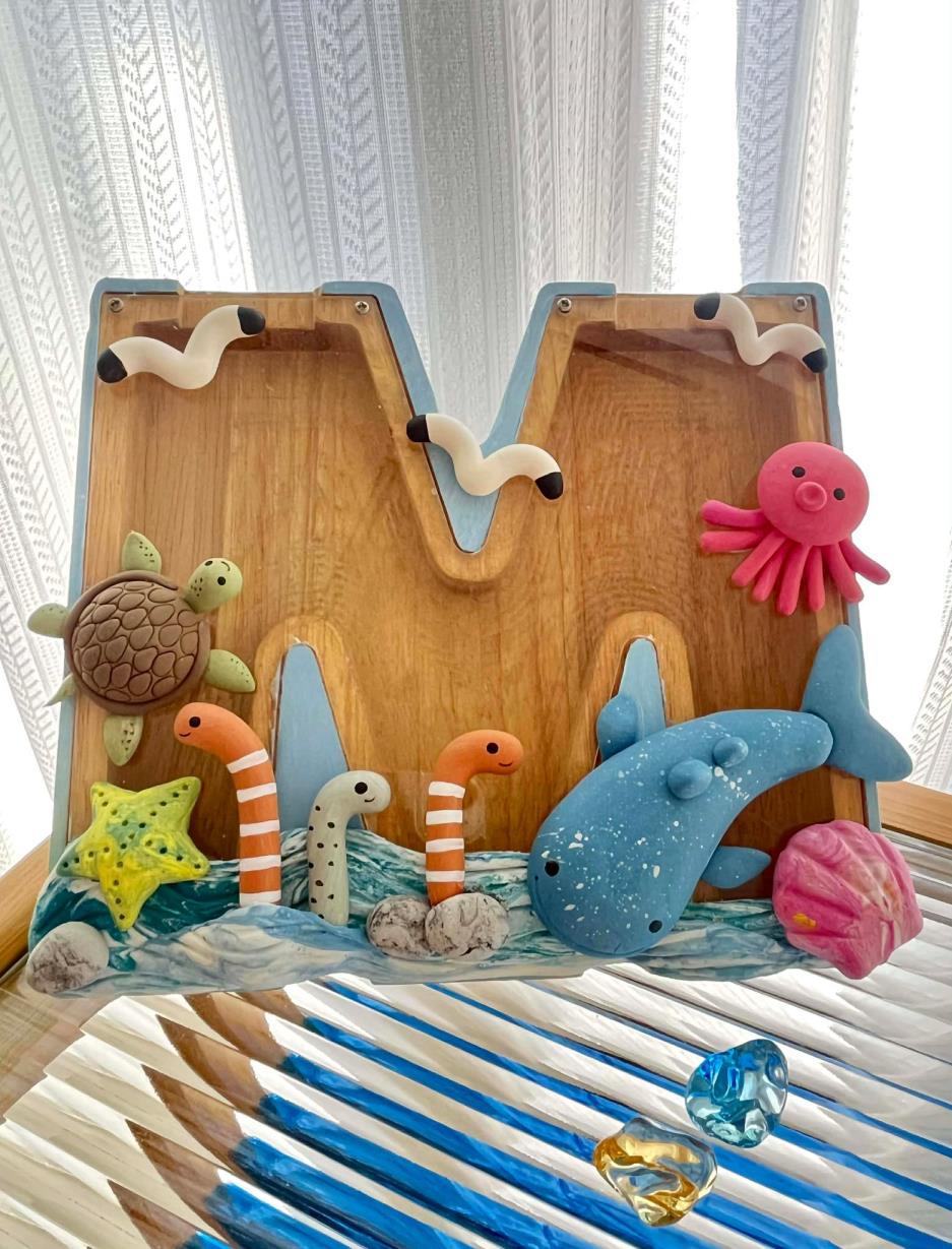 搭配屬於自己的英文字母，結合海洋元素與童趣角色，創作屬於自己的存錢筒作品，把夏日的回憶悄悄收藏在裡面。